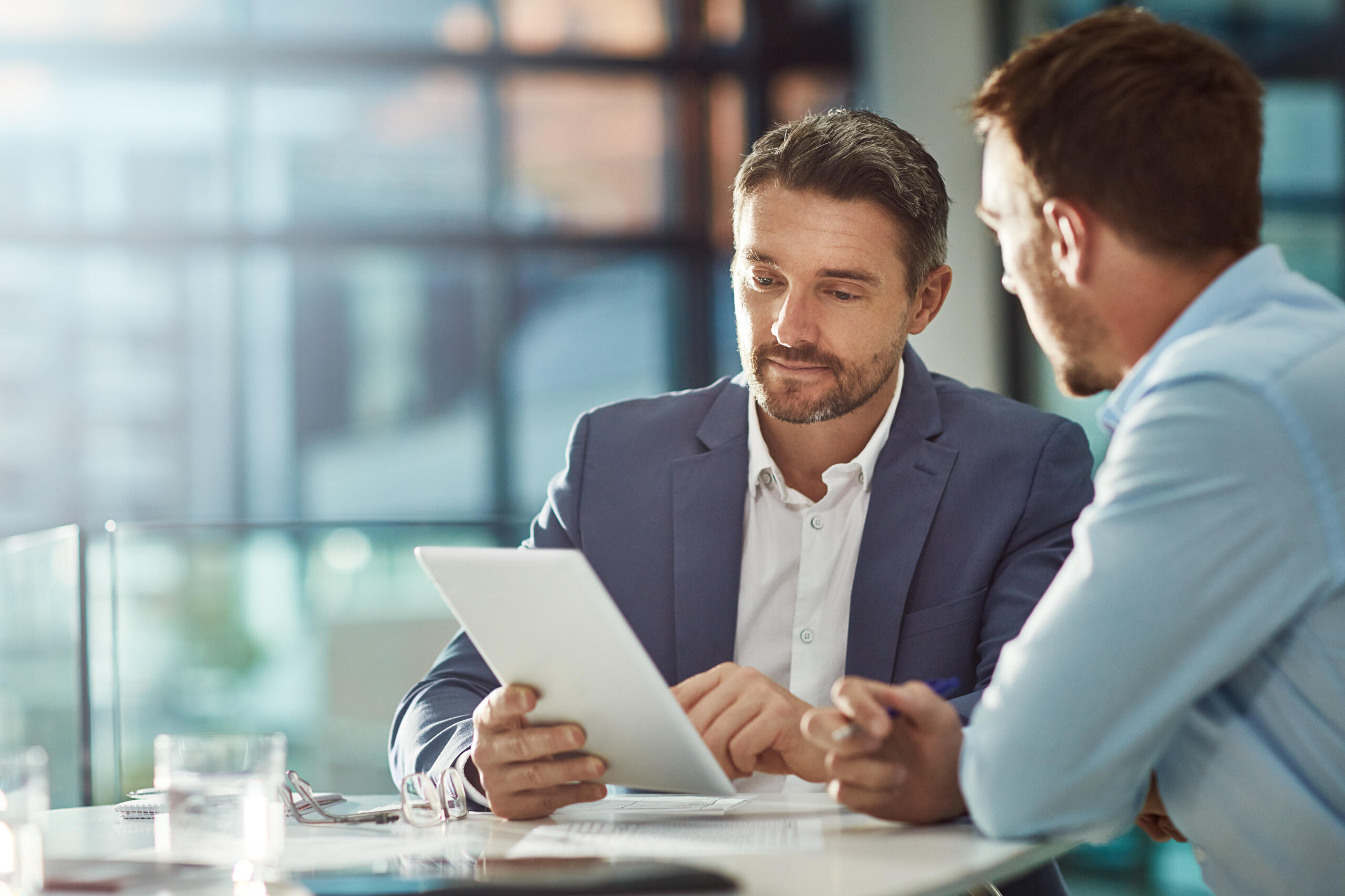 About Us Picture of man sitting with colleague holding a tablet.